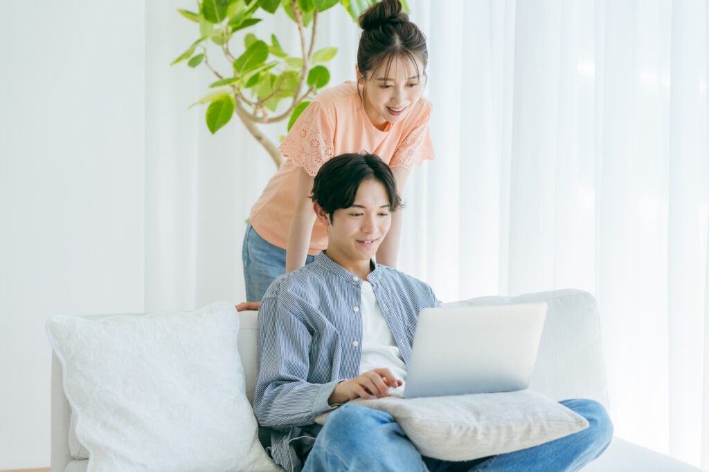 リビングのソファーで白いパソコンを見ている若い夫婦