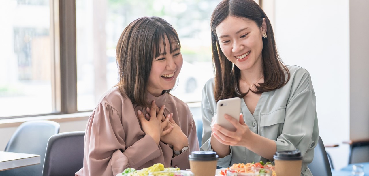 スマホを見ながら笑顔で食事をする２人の女性