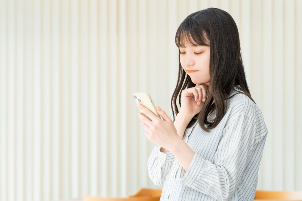 スマホの画面を見つめて考えている女性