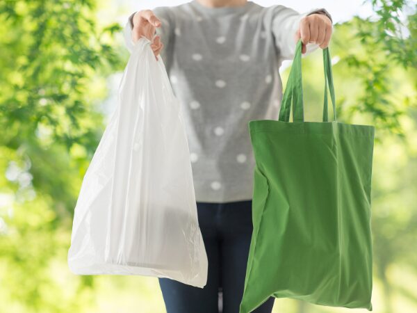 右手に大きめの白いビニール袋と左手に緑色のトートバッグを持ったグレーに白の水玉の服を着た人
