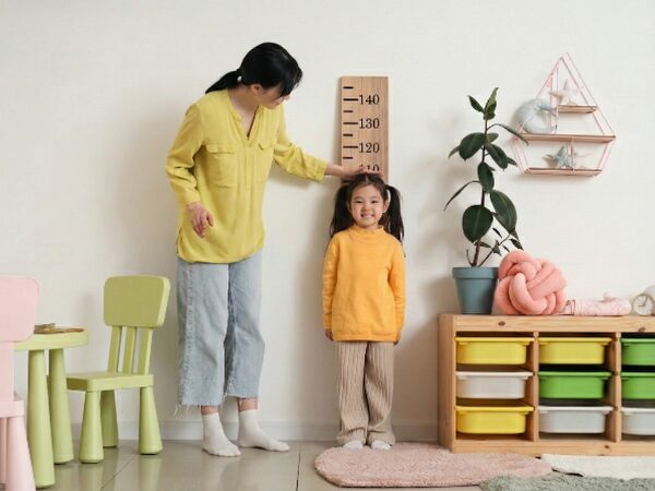 部屋で母親に身長を図ってもらっている5歳の女の子